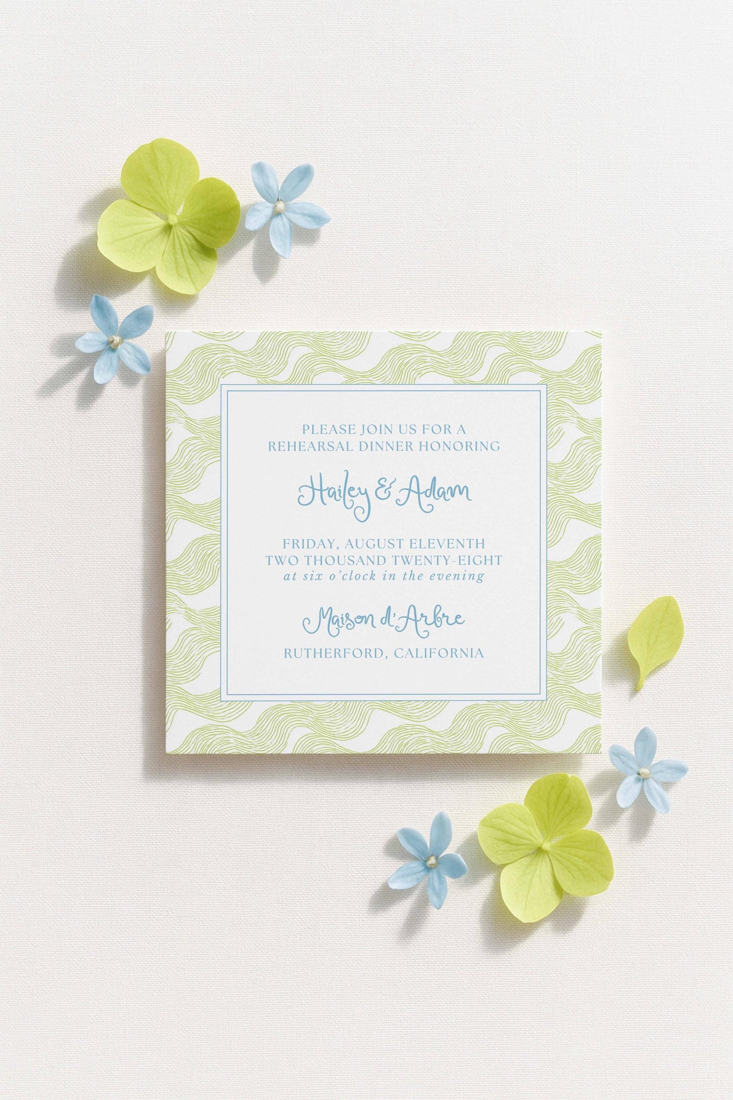 The image is a wedding invitation card with a light green and white color scheme, featuring a floral pattern and blue accents.