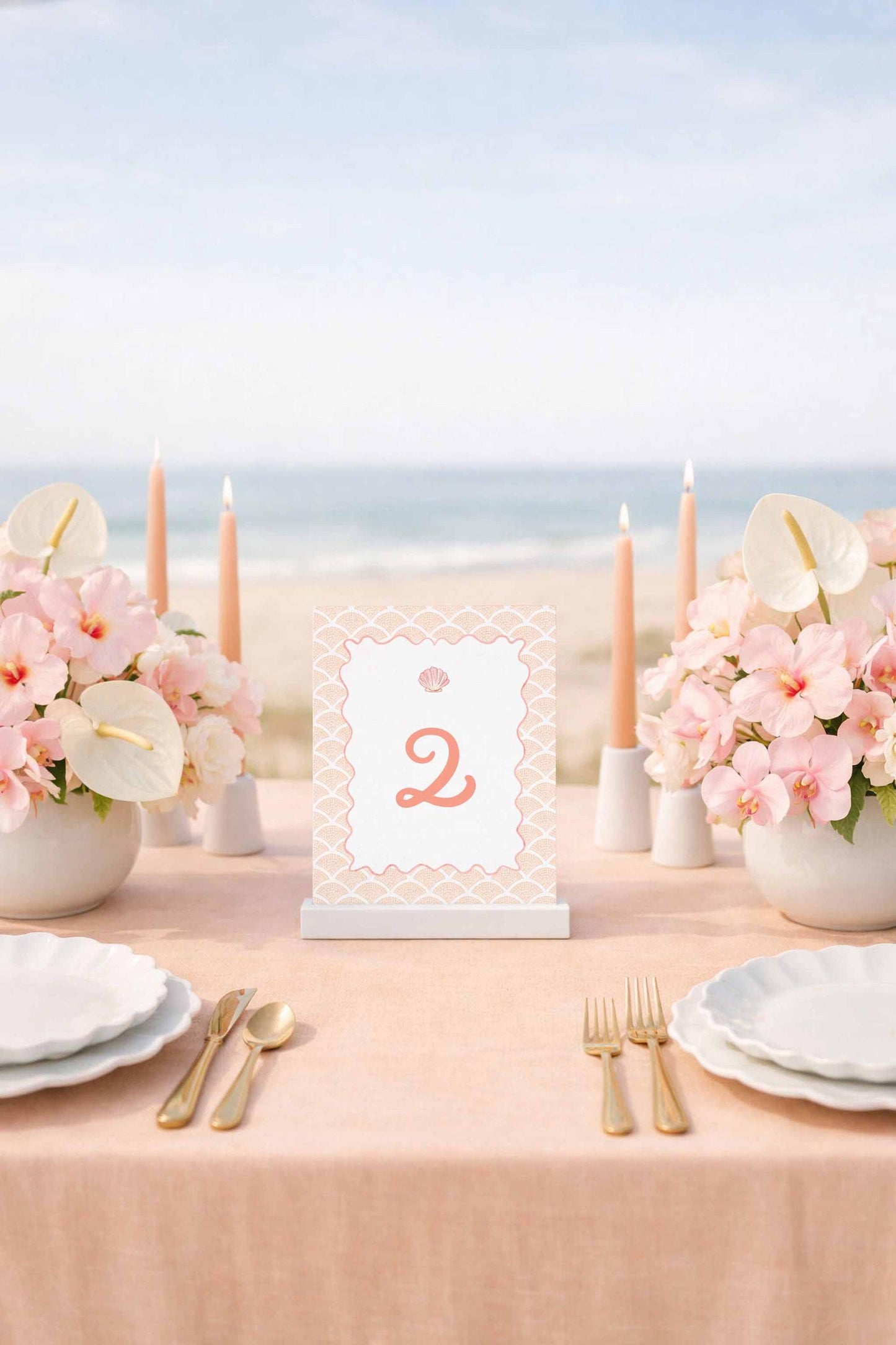 a table set for a formal dining experience, with a tablecloth, plates, silverware, and a centerpiece of pink flowers. The table is positioned near the ocean, creating a serene and picturesque setting.