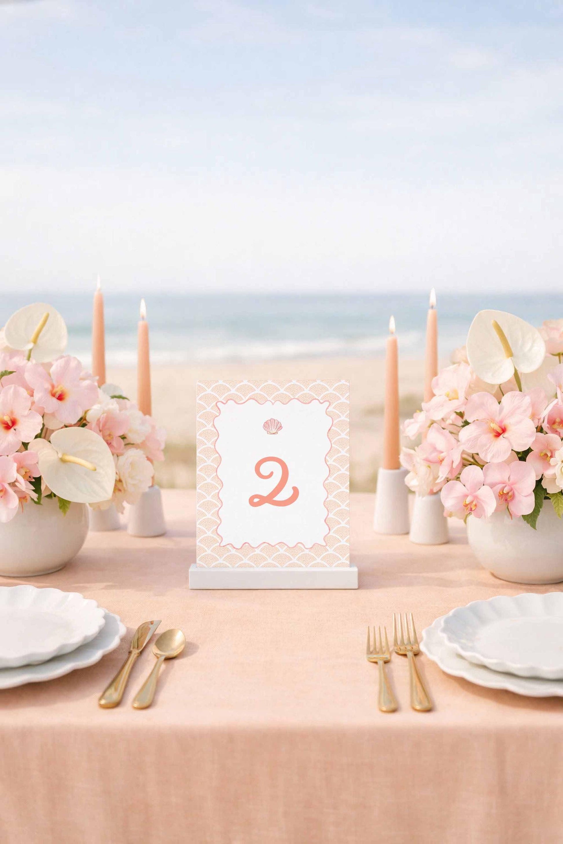 a table set for a formal dining experience, with a tablecloth, plates, silverware, and a centerpiece of pink flowers. The table is positioned near the ocean, creating a serene and picturesque setting.