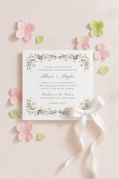 a formal invitation card with floral designs and a white ribbon bow, surrounded by pink and green flowers on a light pink background.