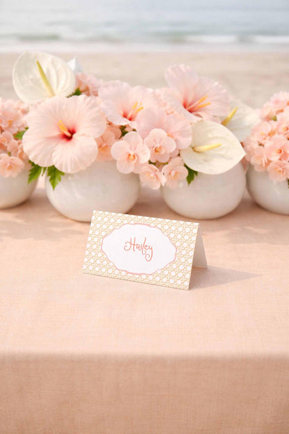 A table with a white tablecloth and a card holder displaying the name "Haley" in the center. Behind the card holder are white vases filled with pink flowers, creating a beautiful floral arrangement.