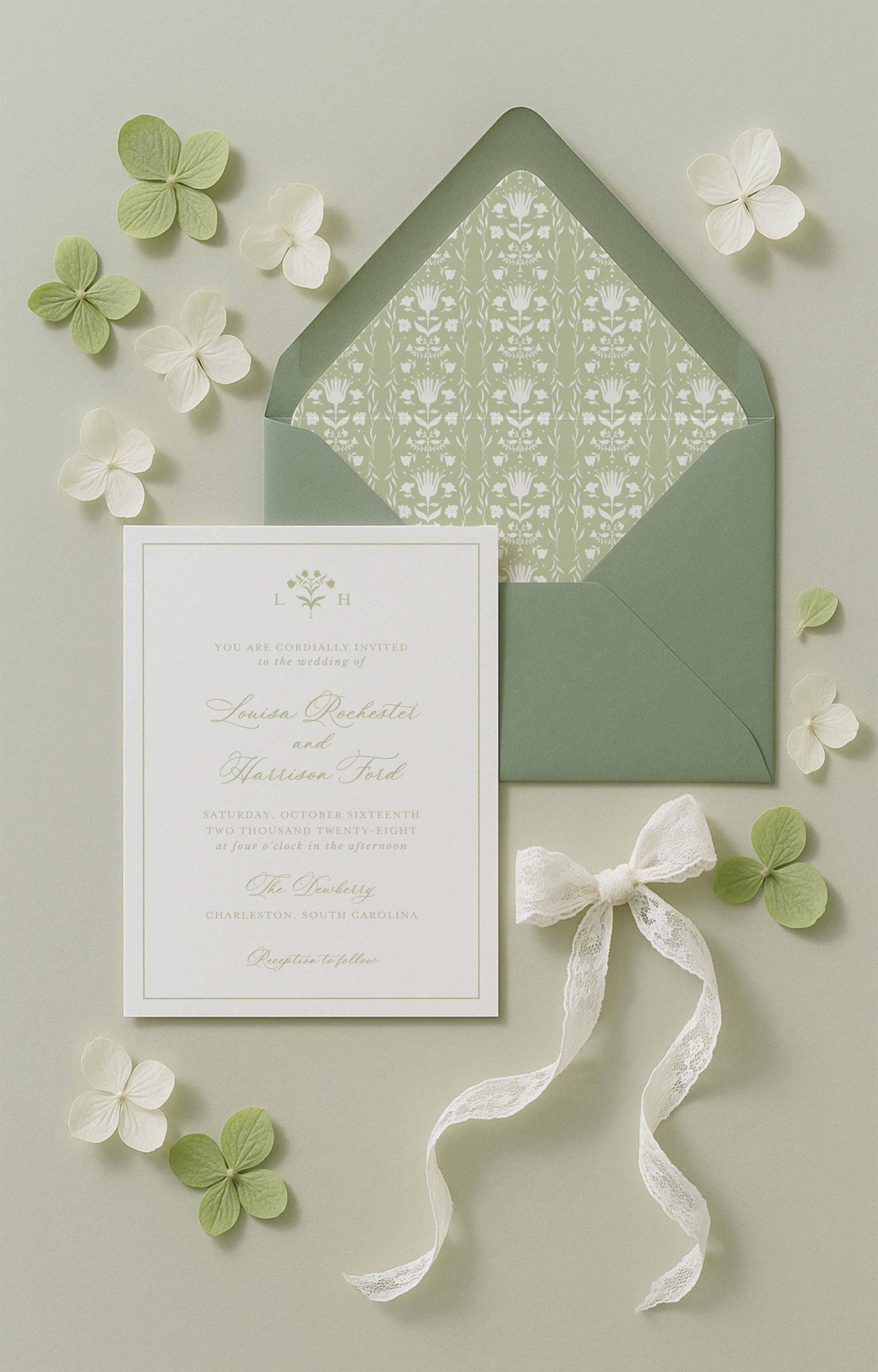a wedding invitation card with a green envelope, white flowers, and a white ribbon.
