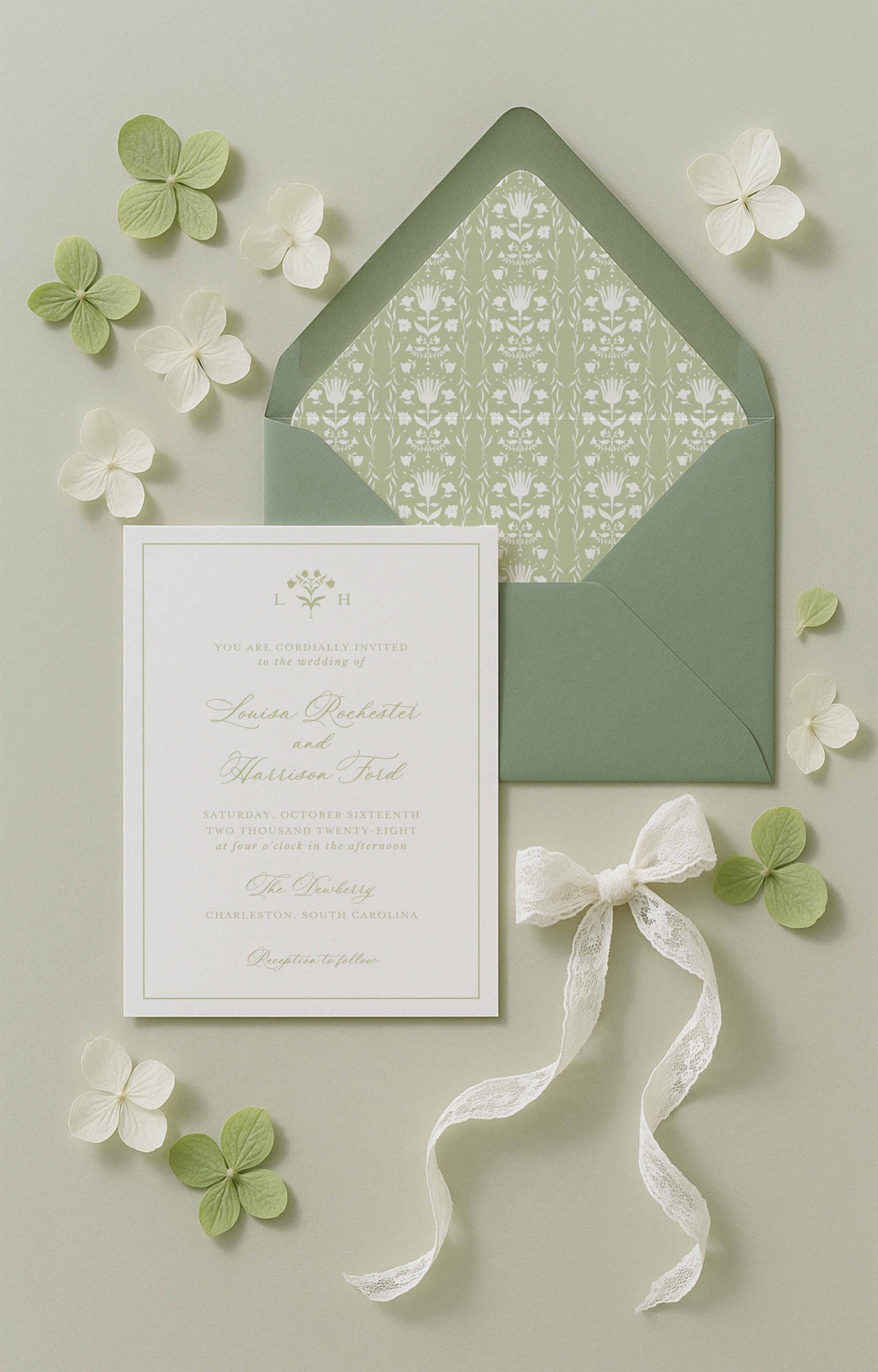 a wedding invitation card with a green envelope, white flowers, and a white ribbon.