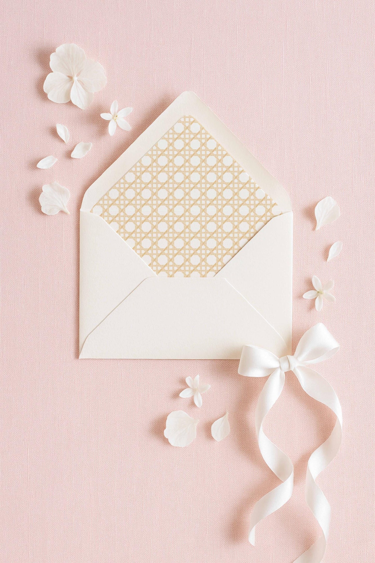 a white envelope with a gold pattern, a white ribbon, and white flowers on a pink background.
