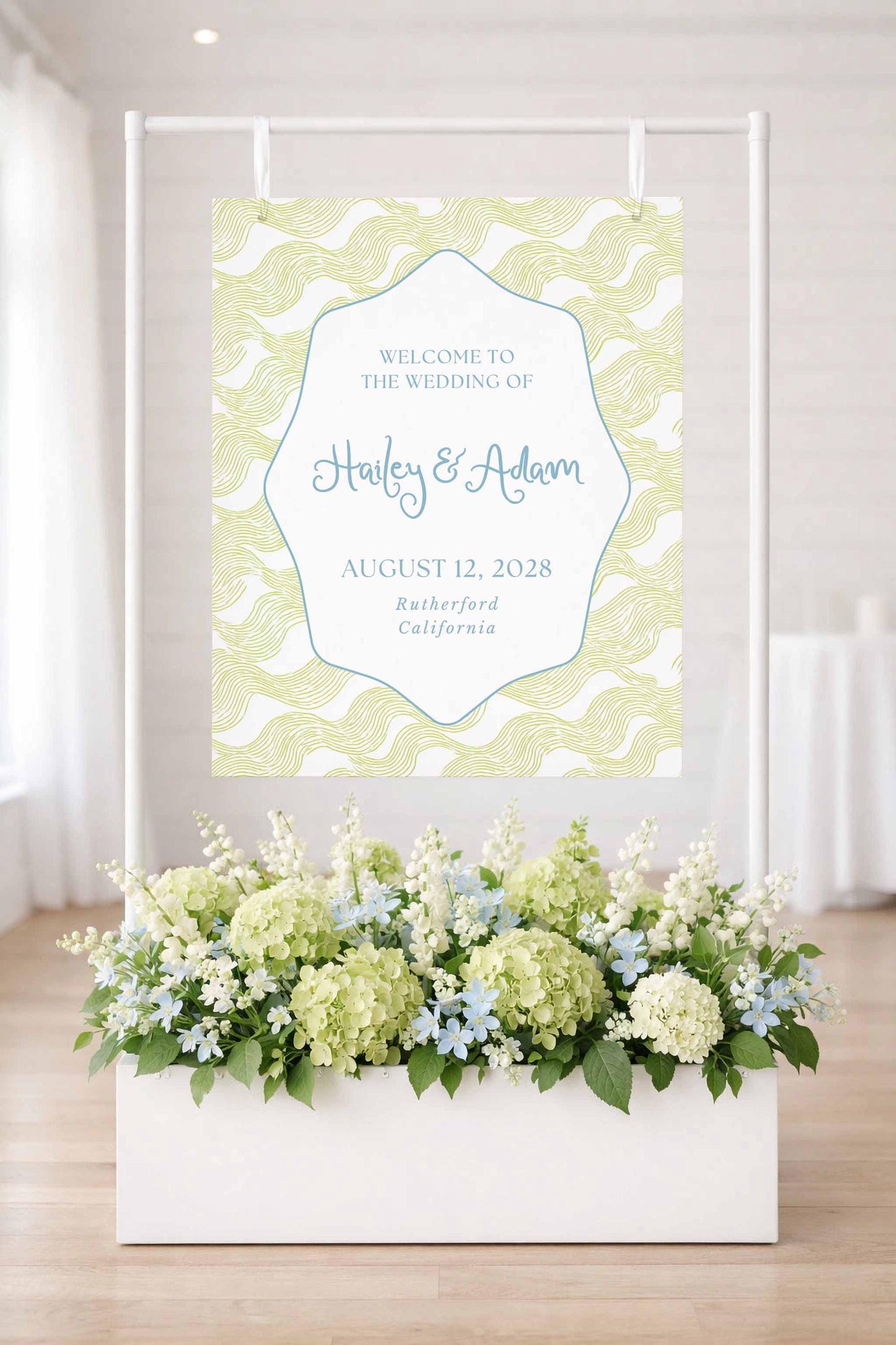 a wedding invitation sign with a floral arrangement in a white planter below it.