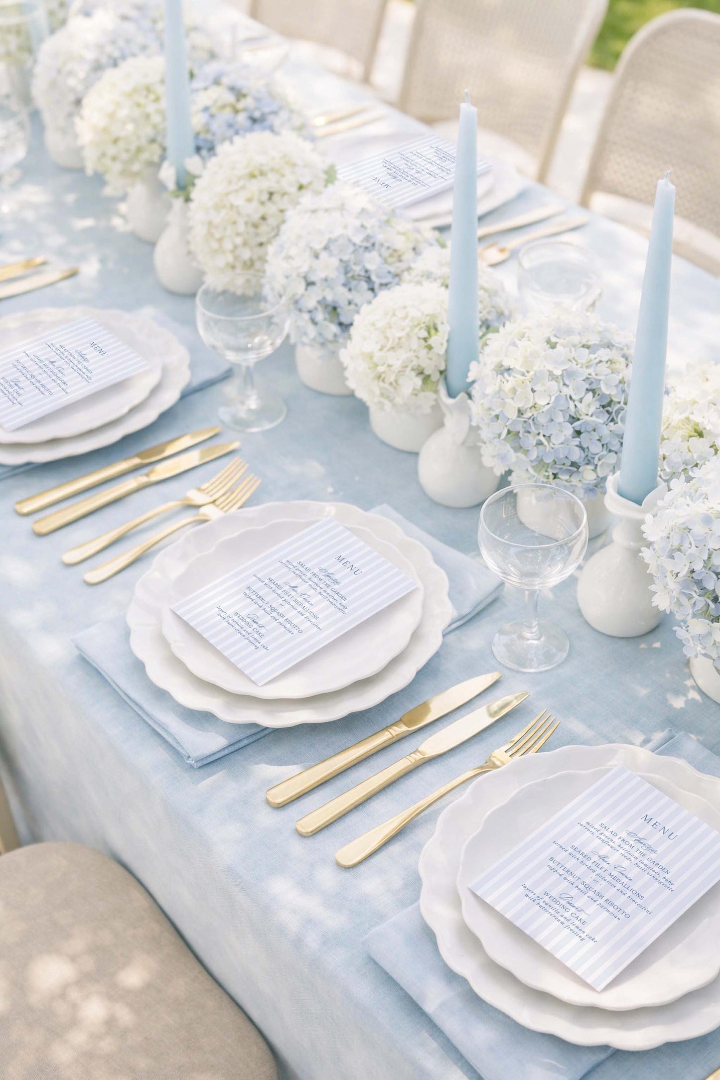 a beautifully set dining table with white plates, gold cutlery, and elegant floral arrangements. The table is set for a formal meal, with place settings and tableware arranged neatly.