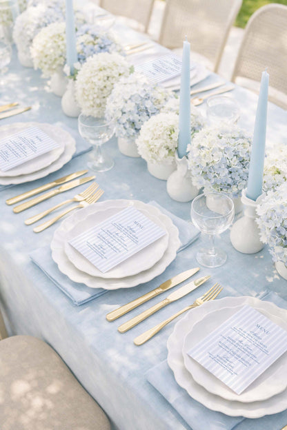 a beautifully set dining table with white plates, gold cutlery, and elegant floral arrangements. The table is set for a formal meal, with place settings and tableware arranged neatly.