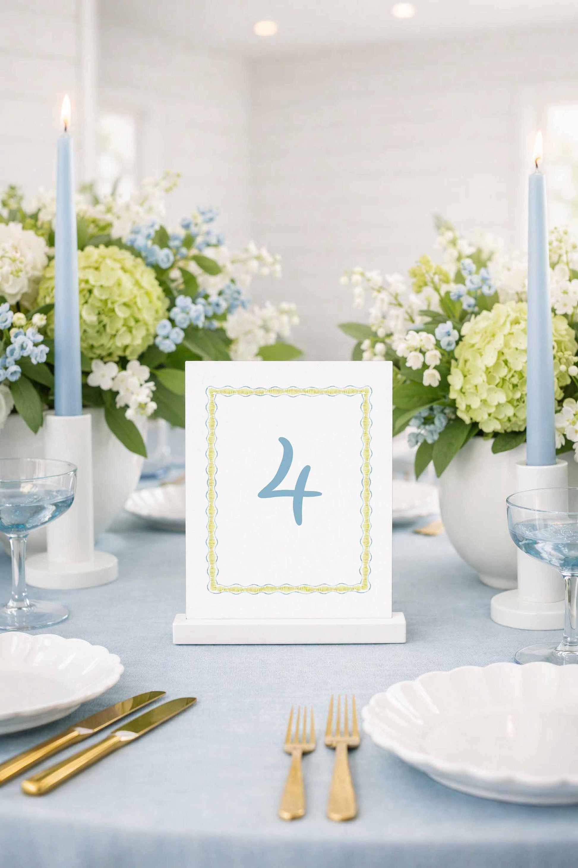 a table setting with a white tablecloth, a white table number card displaying the number '4', and various tableware items such as plates, glasses, and cutlery.