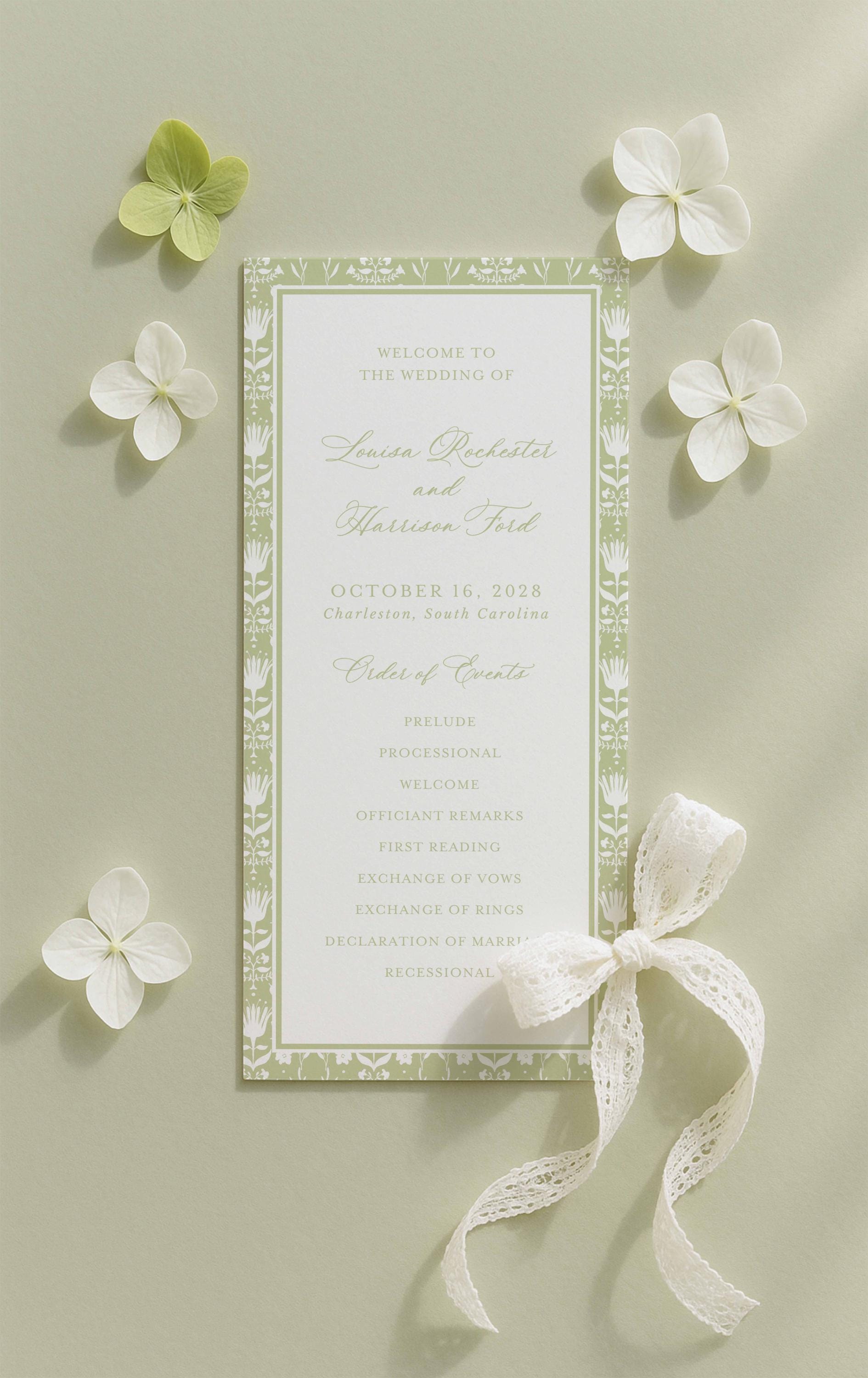a wedding invitation card with a green and white color scheme, surrounded by white flowers and a white ribbon.