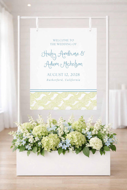 a white wedding sign with a floral arrangement in a white planter below it.
