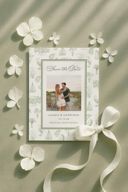 Save the Date card with southern toile artwork surrounding a customizable text area and optional engagement photo. Displayed alongside white flower petals and a satin ribbon on green fabric. The toile design includes palmettos, egrets, oysters, sailboats, oak trees, and marsh elements. Canva editable, printable, and includes a matching toile envelope liner for a cohesive wedding stationery suite. Perfect for coastal and Lowcountry weddings.