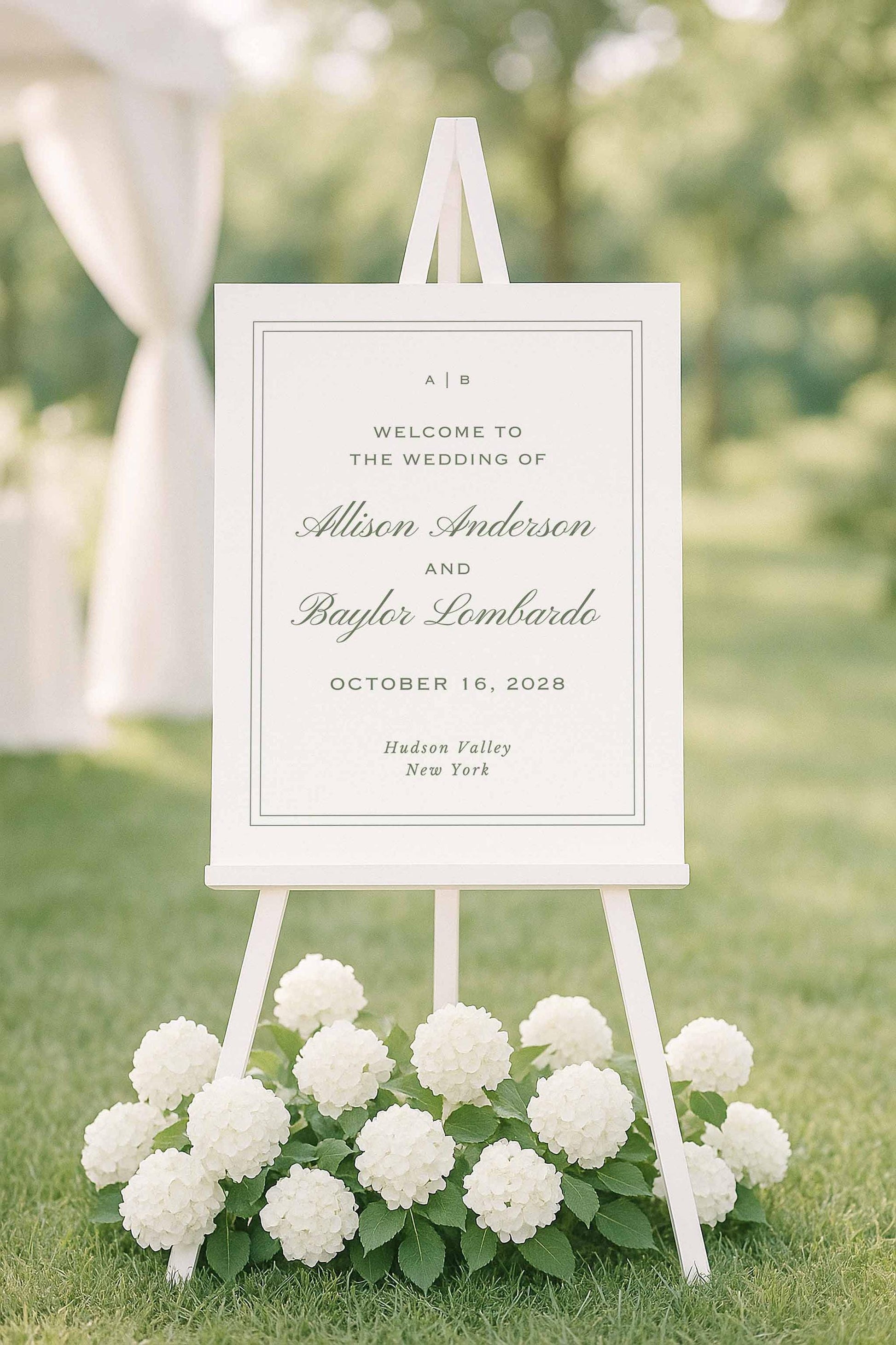 Green striped watercolor welcome sign displayed on an easel surrounded by white hydrangeas outdoors.