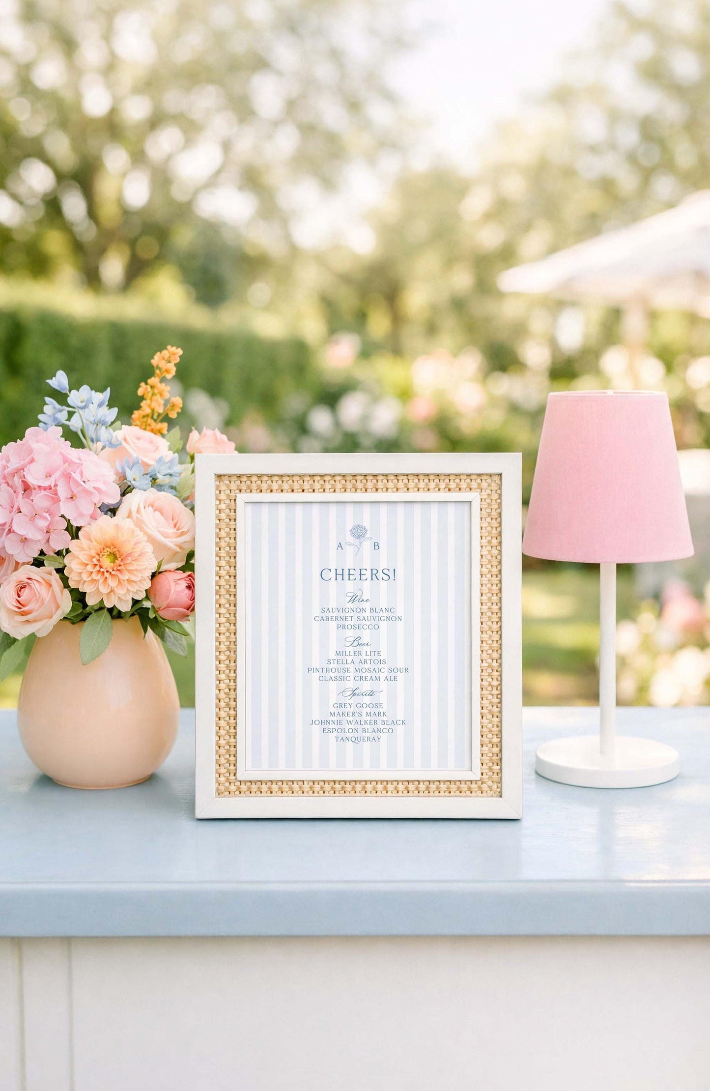 a framed menu with a blue and white color scheme, placed on a table next to a vase of pink and blue flowers, and a pink lamp.