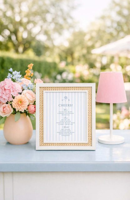 a framed menu with a blue and white color scheme, placed on a table next to a vase of pink and blue flowers, and a pink lamp.