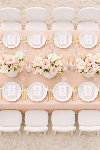 a beautifully set dining table with white plates, gold cutlery, and a vase of pink and white flowers. The table is surrounded by white chairs, creating an elegant and inviting atmosphere.