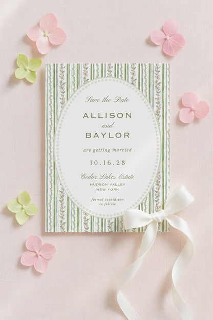 a wedding invitation card with a green and white striped border, a white ribbon, and pink flowers surrounding it.