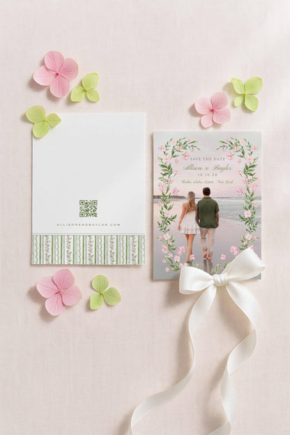a white card with a floral design and a ribbon, surrounded by pink and green flowers, as well as a white ribbon.