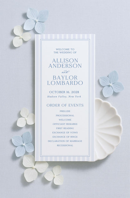 a wedding invitation card with a blue and white color scheme, placed on a light blue background with white flowers scattered around it.