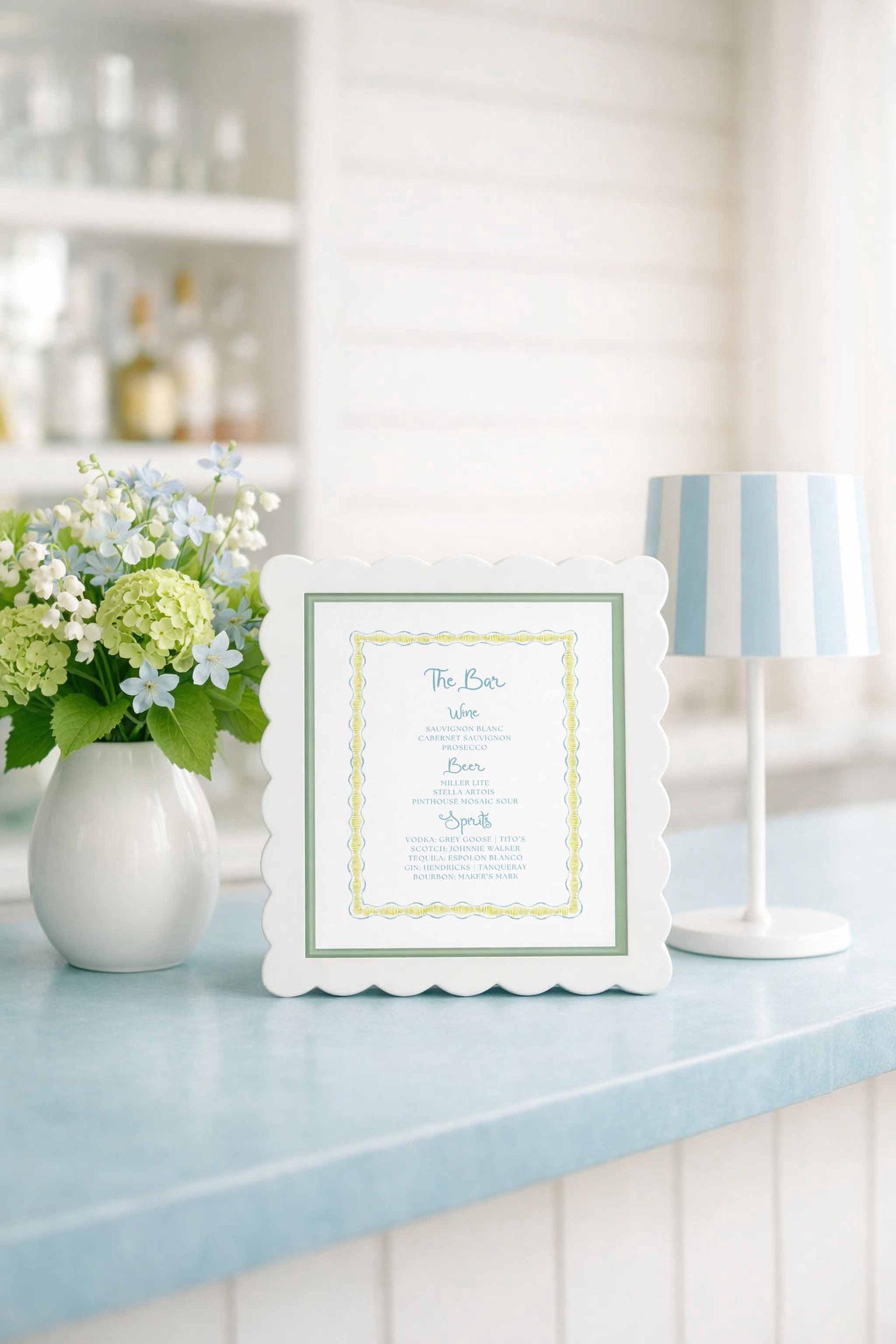 a white framed menu with a blue border, placed on a blue countertop next to a vase of white and green flowers.