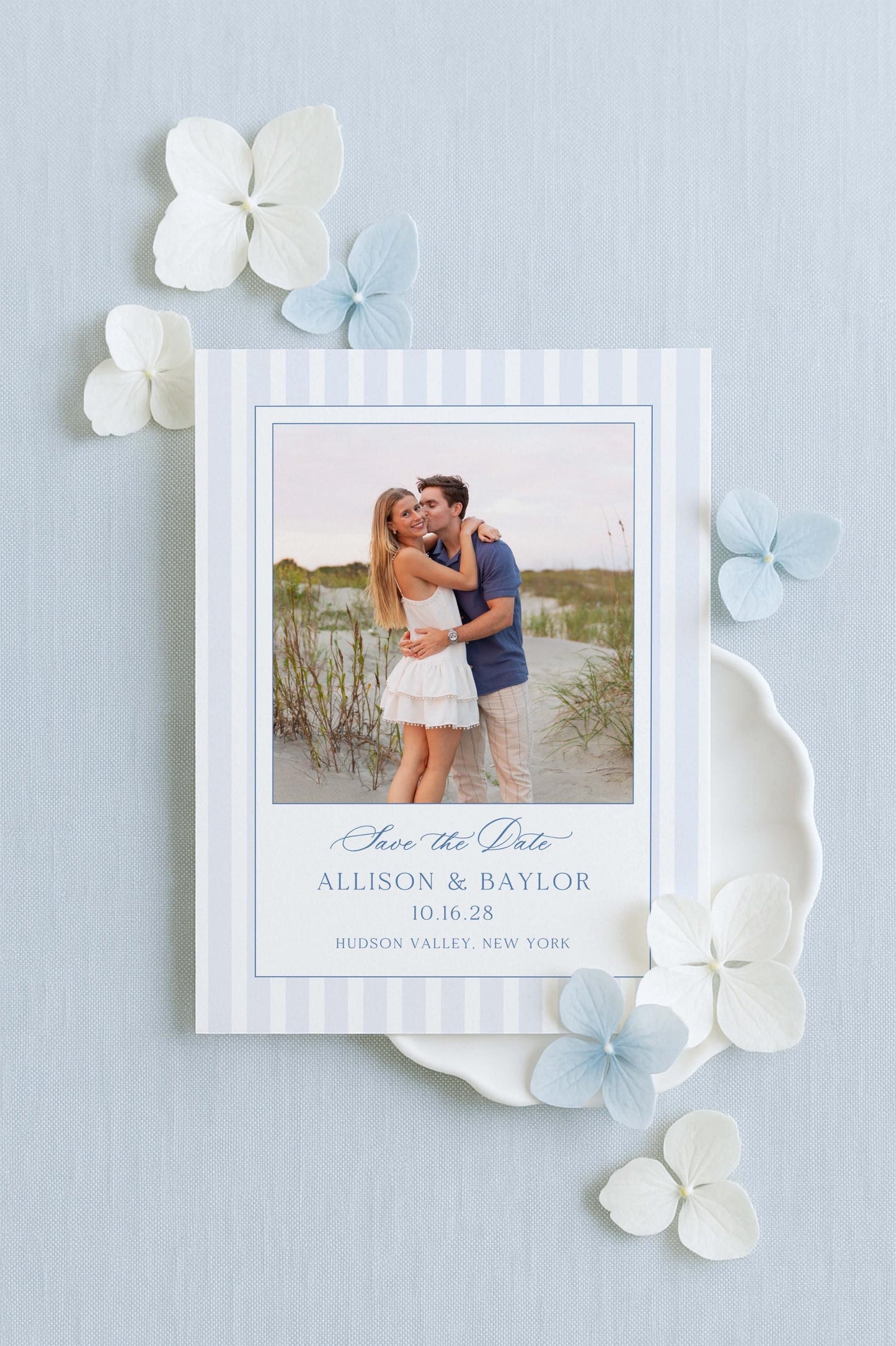 A white wedding invitation card with a photo of a couple embracing, surrounded by white and light blue flowers.