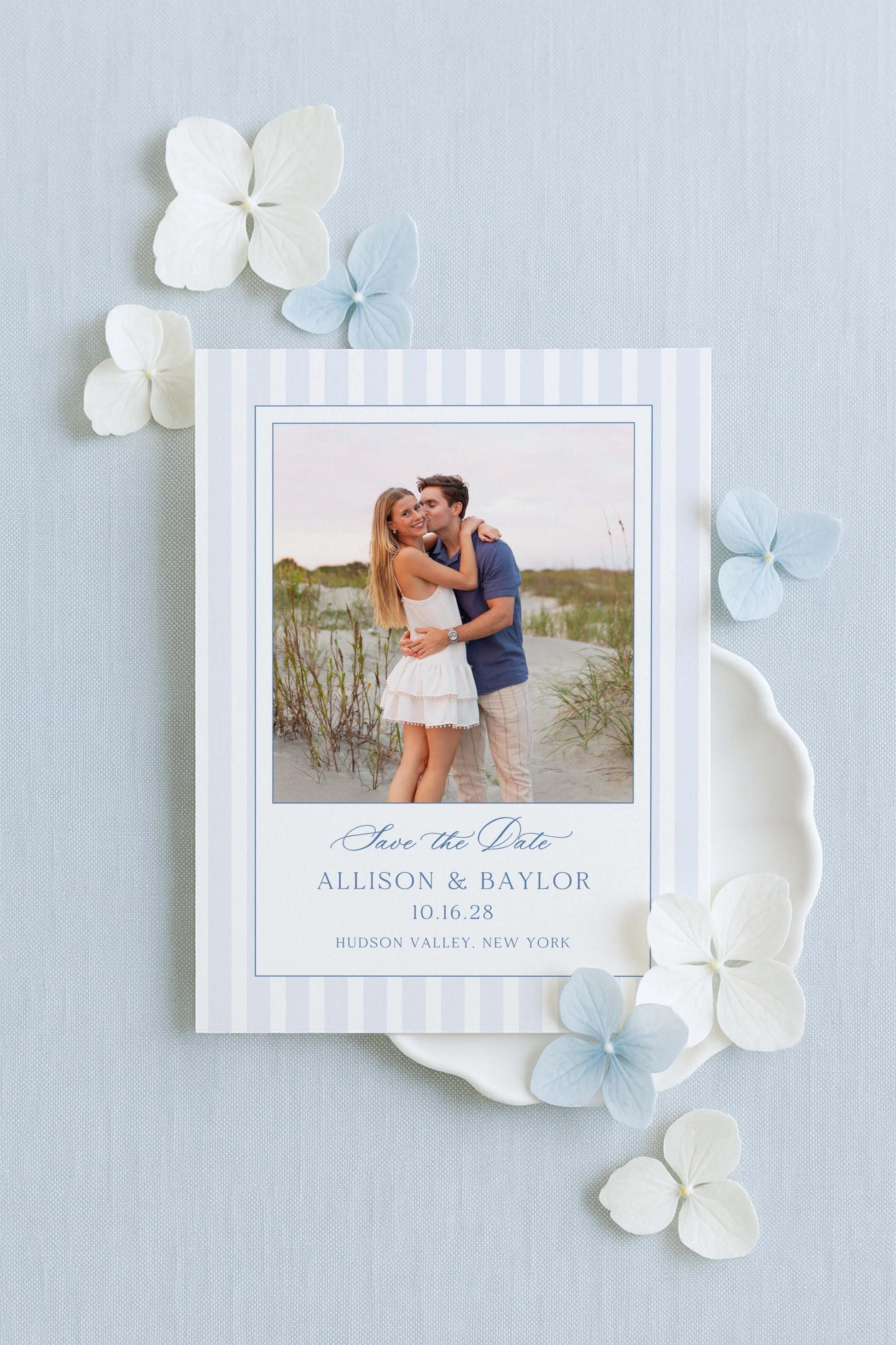 A white wedding invitation card with a photo of a couple embracing, surrounded by white and light blue flowers.