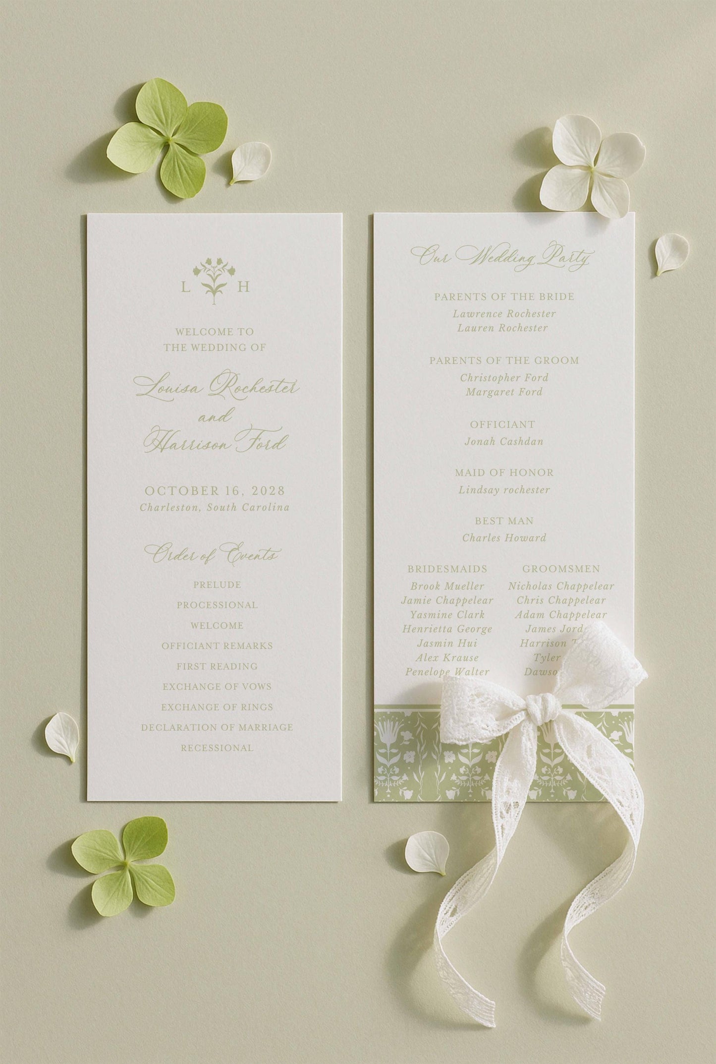 a wedding invitation card with a white background and green leaves. The card is placed on a light green background with white flowers scattered around it.