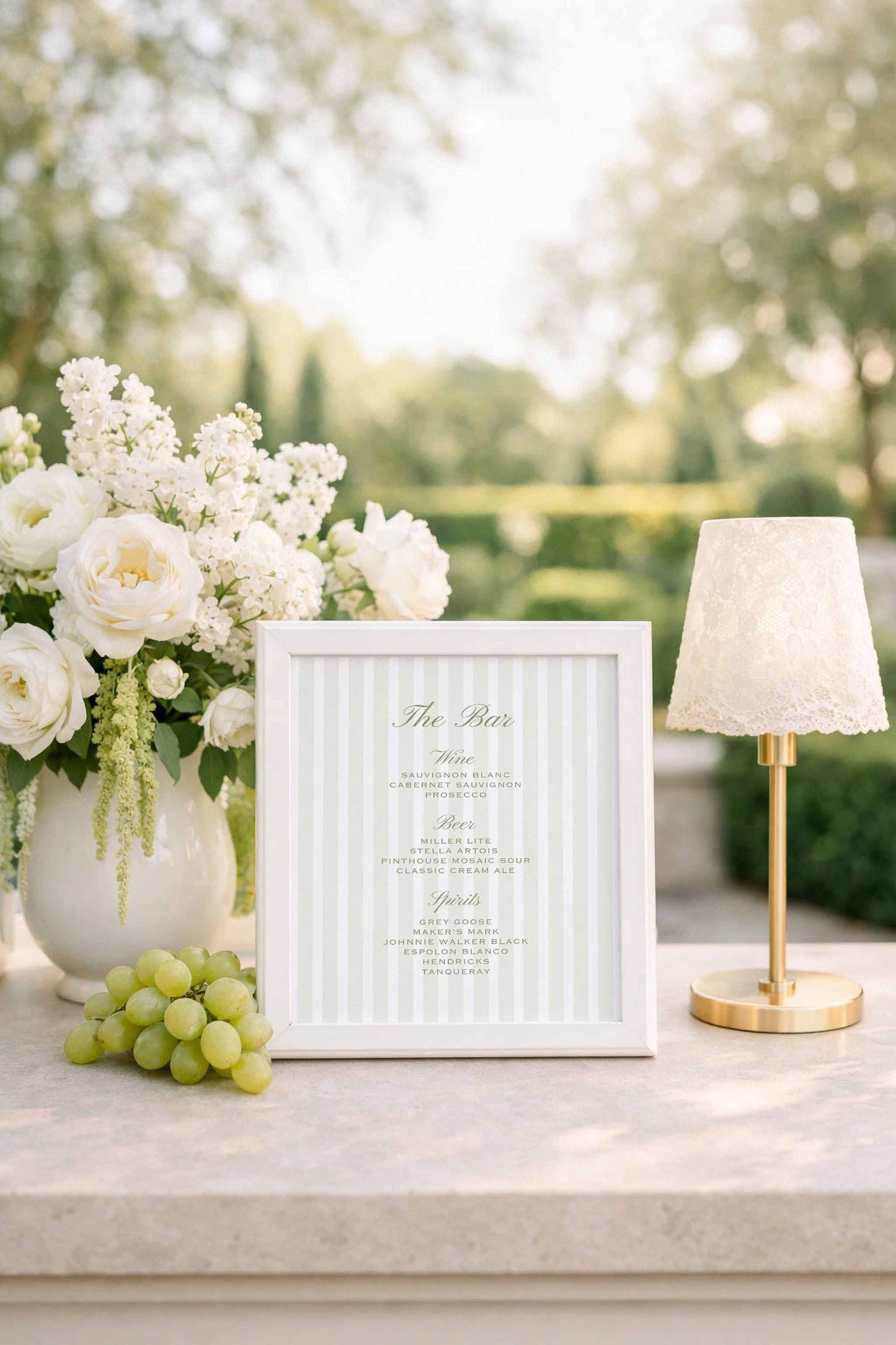 a white framed menu with a green stripe, placed on a table next to a vase of white flowers and a small lamp.