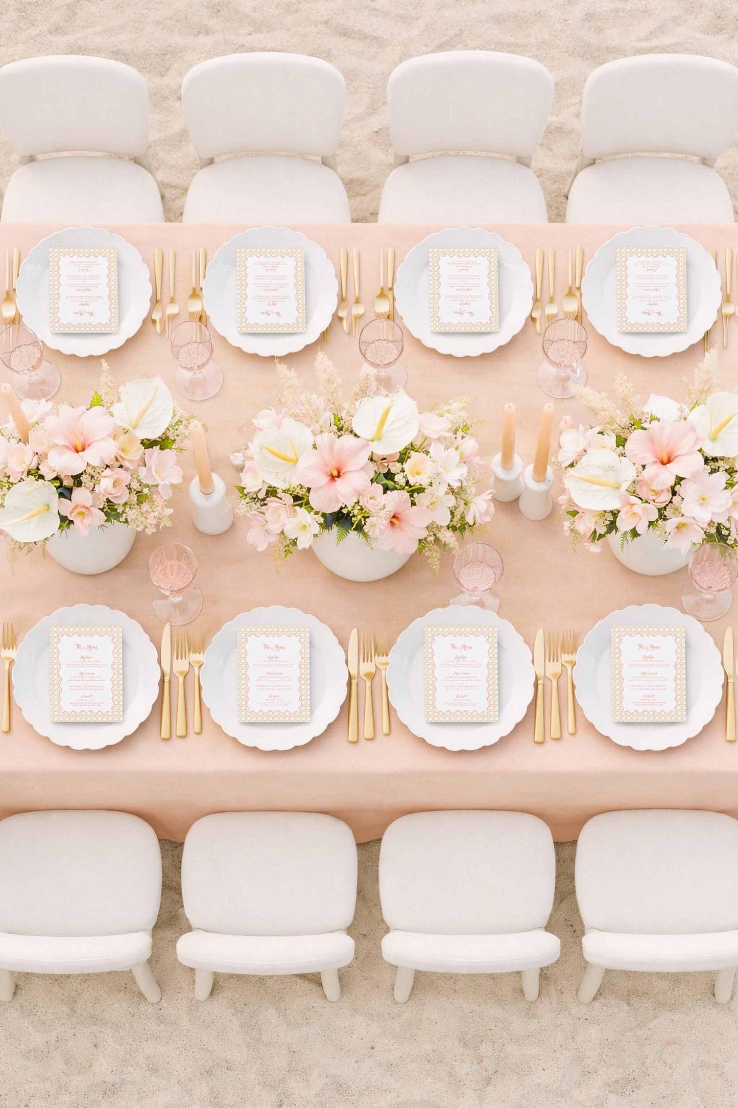 a beautifully set dining table with white plates, gold cutlery, and a vase of pink and white flowers. The table is surrounded by white chairs, creating an elegant and inviting atmosphere.
