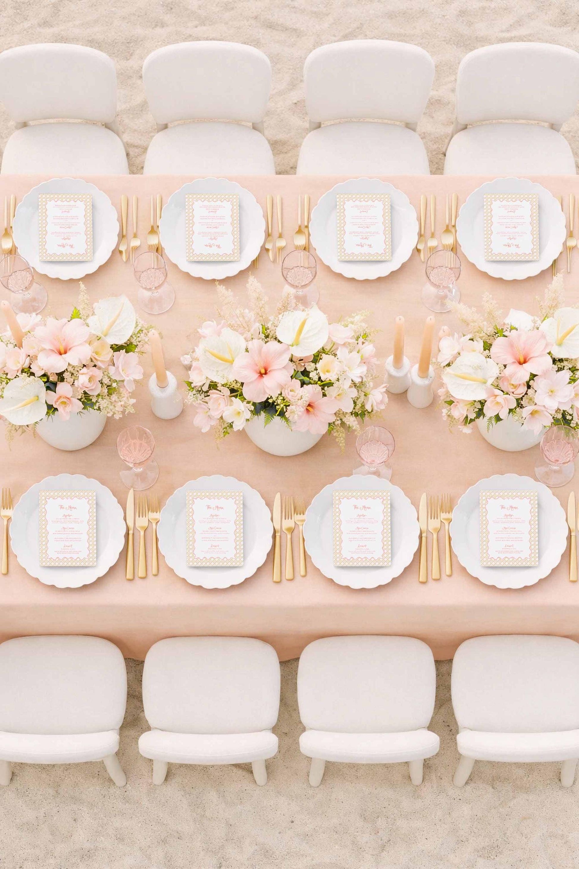 a beautifully set dining table with white plates, gold cutlery, and a vase of pink and white flowers. The table is surrounded by white chairs, creating an elegant and inviting atmosphere.