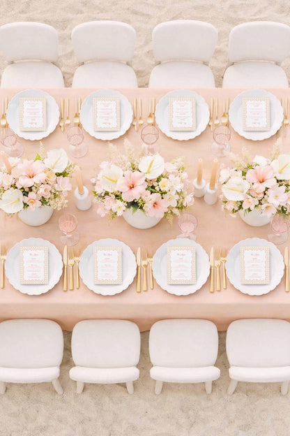 a beautifully set dining table with white plates, gold cutlery, and a vase of pink and white flowers. The table is surrounded by white chairs, creating an elegant and inviting atmosphere.
