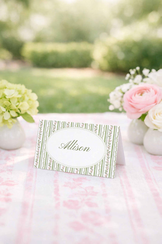 A table with a white tablecloth and a green and white striped place card in the center, surrounded by white vases with pink and white flowers.